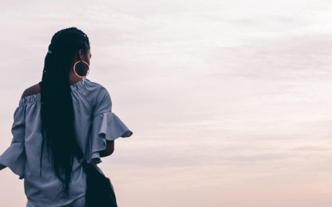 Image of a Back woman staring out at the pink sky. Representing someone who could benefit from ACT therapy in Atlanta, Georgia. With support of a therapist ACT for anxiety can give you freedom.