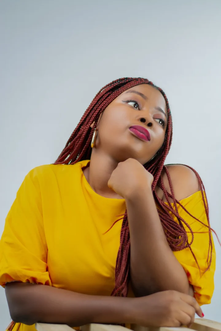 Image of Black woman with anxiety wear a yellow shirt with hand under chin and strained expression. She looks tired.