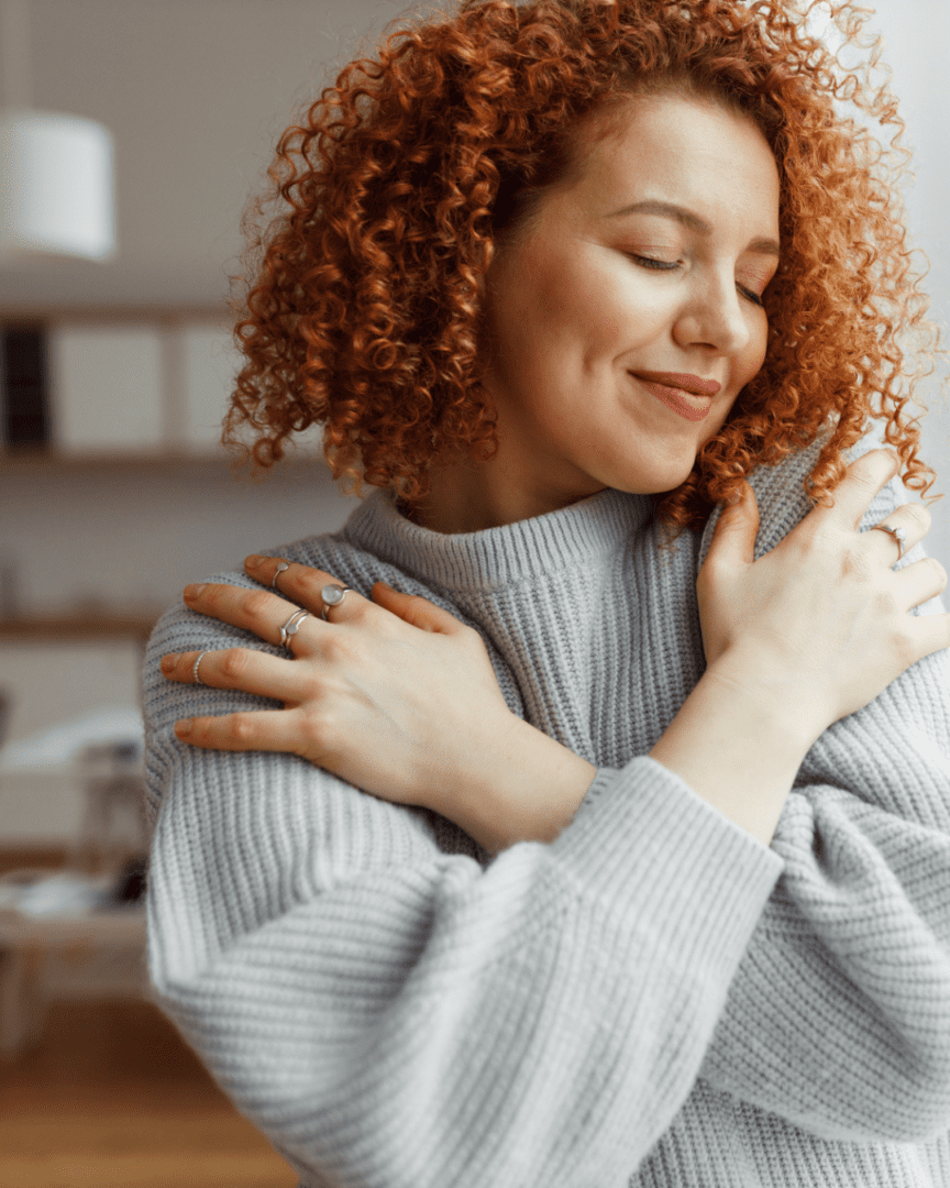 Woman with red hair hugging herself, offering self-compassion to manage nervousness with grace.